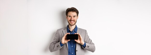 Free photo ecommerce and online shopping concept happy guy in business suit showing empty smartphone screen hor