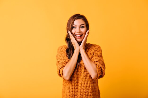 Ecstatic beautiful woman touching her face. Studio portrait of smiling carefree girl isolated on yellow.