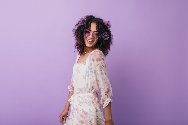 Ecstatic black girl in trendy dress posing with happy smile. glad african female model wears flowers in wavy hair.