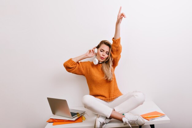 Ecstatic blonde woman with nude make-up holding headphones and enjoying music during break in office