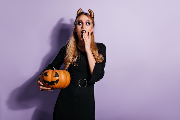 Ecstatic female vampire thinking about something evil. witch in black dress holding pumpkin.