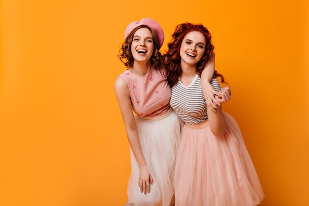 Ecstatic friends embracing on yellow background. Glamorous girls in good mood laughing at camera.