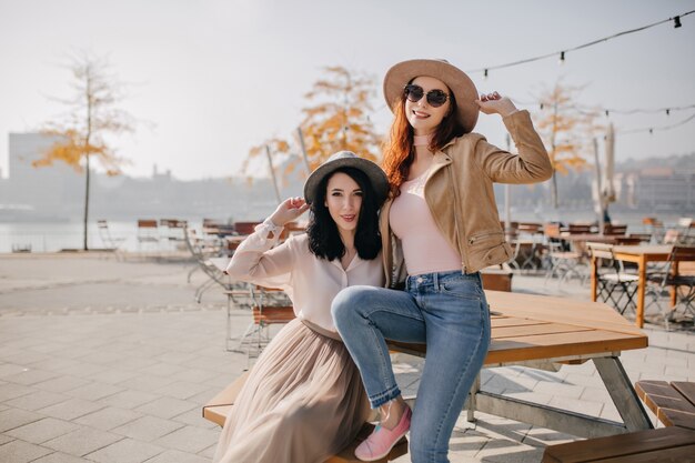 Ecstatic ginger woman in pink shoes sitting on wooden table in sunny day and laughing