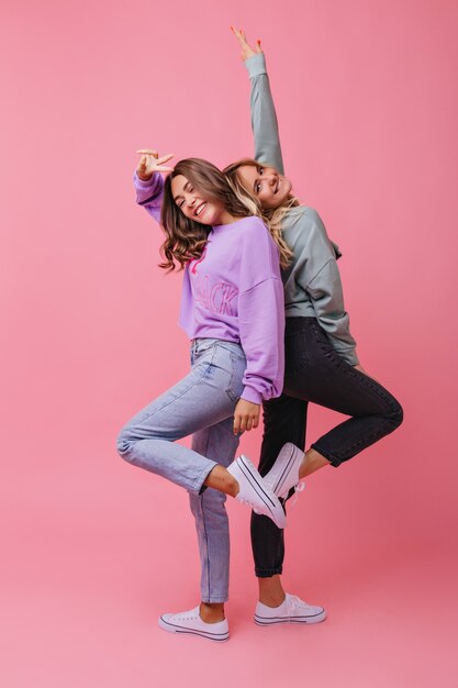 Ecstatic girls in trendy clothes enjoying portraitshoot. Enthusiastic female model expressing positive emotions and smiling.