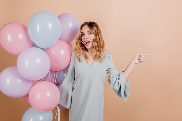 Ecstatic short-haired lady in blue gown posing with party balloons