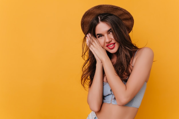 Ecstatic tanned girl in vintage tank-top and hat smiling to camera