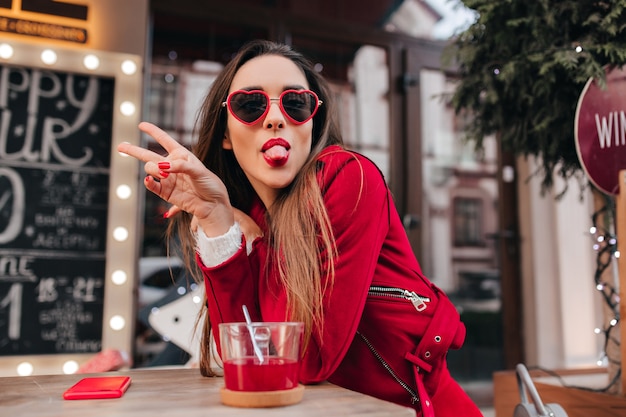 Estatico giovane modello femminile in occhiali rossi in posa con la lingua fuori