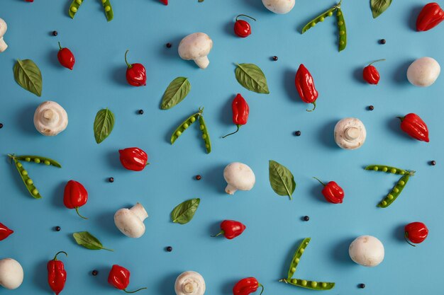 Edible healthy nutrient vegetables on blue background. White champignons, green peas, red pepper and peppercorns can be added to cook delicious dish. Ingredients for mushroom curry or cream soup