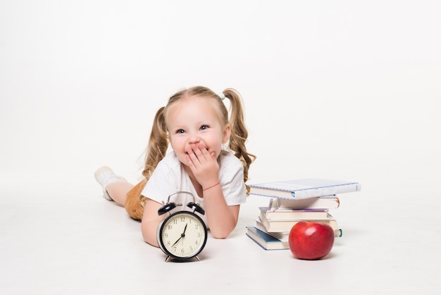 Бесплатное фото Концепция образования и школы. улыбающаяся маленькая студентка с книжными часами и яблоком, лежащим на полу