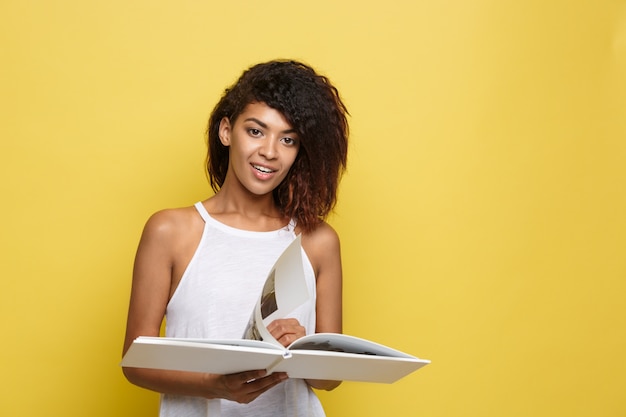 Free photo education concept - portrait of african american woman reading a book. yellow studio background. copy space.