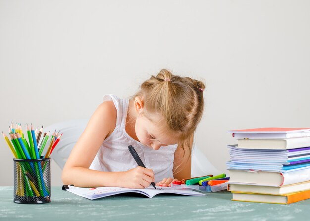 education concept with school supplies side view. little girl drawing on copybook.