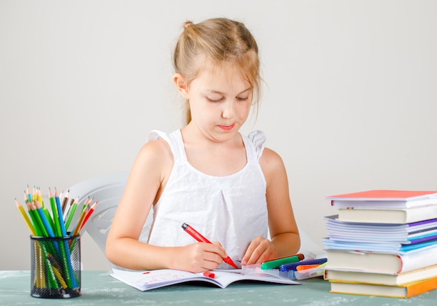 Education concept with school supplies side view. little girl drawing on copybook.