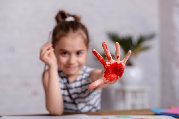 교육, 학교, 예술 및 그림 개념 - 학교에서 손으로 칠한 손을 보여주는 웃는 어린 학생 소녀. 그리기용 페인트