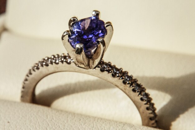 Egagement ring with blue precious stone on white pillow 