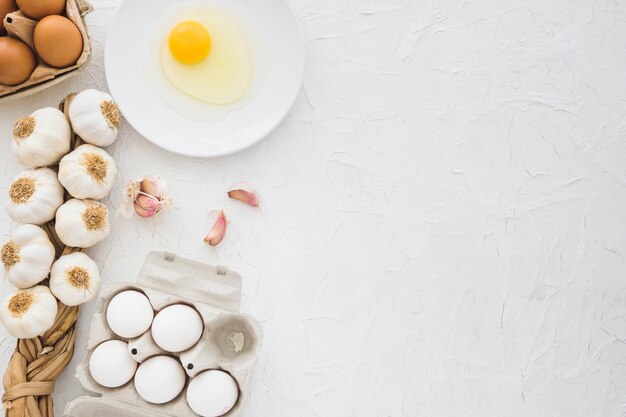 Egg carton and yolk with garlic braid on white textured backdrop