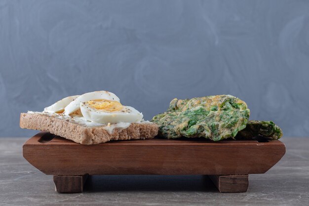 Egg cutlets with greens and toast on wooden board.