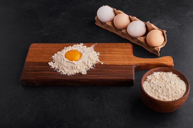 Egg and flour mixed with each other on wooden board. 