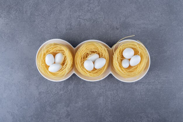 Egg noodle nests with white candies in bowls.