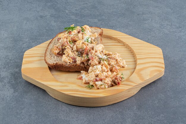Egg salad and bread on wooden plate.