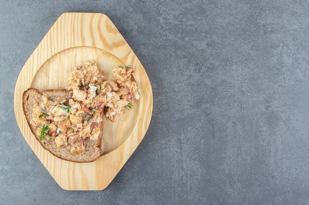 Egg salad and bread on wooden plate.