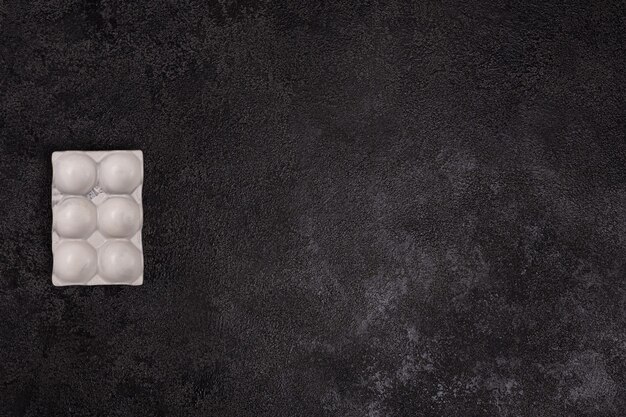 Egg stand made of white concrete on a black textured background.