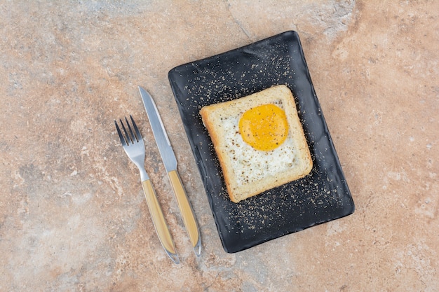 Egg toast with spices on black plate with cutlery