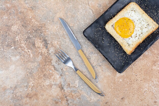 Egg toast with spices on black plate with cutlery