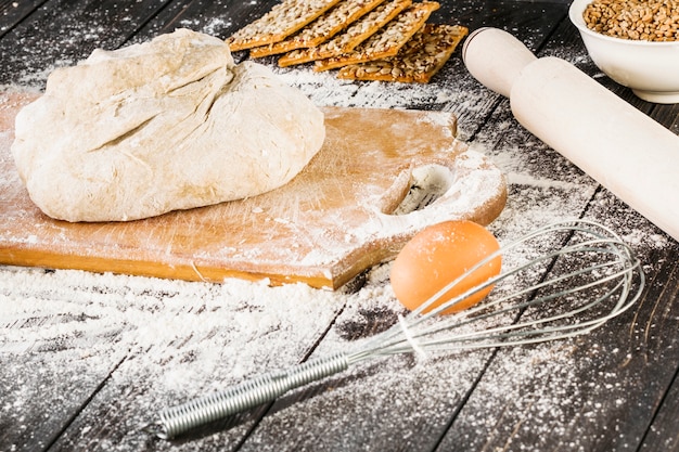 Egg and whisker near the knead dough on chopping board