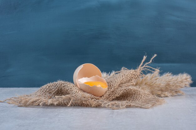 Egg yolk in a broken shell on a piece of cloth on marble table.