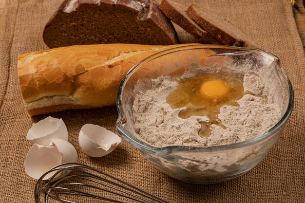 Egg yolk on the flour. Eggshells, baguette and rye bread slices and hand mixer on a piece of burlap.