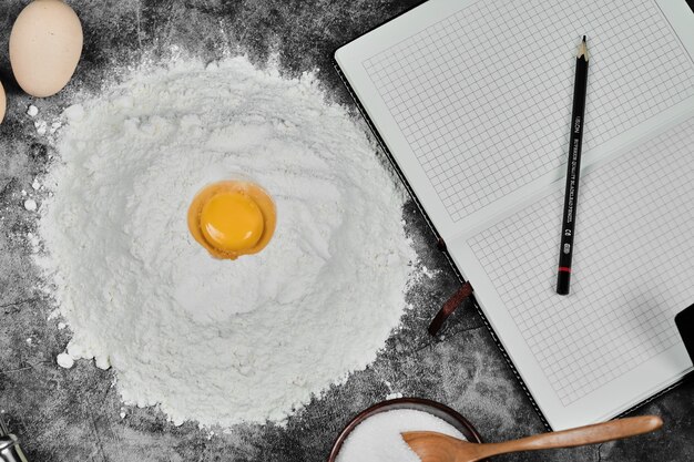 Egg yolk on flour, notebook and pencil on stone table.