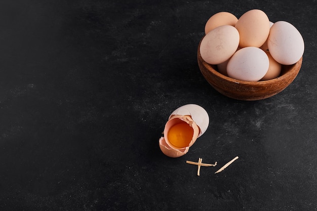 Egg yolk inside a broken eggshell with a wooden cup of eggs aside. 