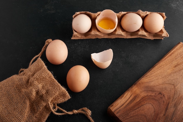 Free photo egg yolk inside eggshell on black background in the cardboard tray.