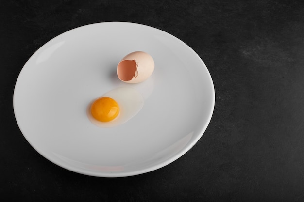 Egg yolk in a white plate with eggshell around.