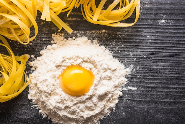 Egg yolk with flour and uncooked tagliatelle on wooden backdrop