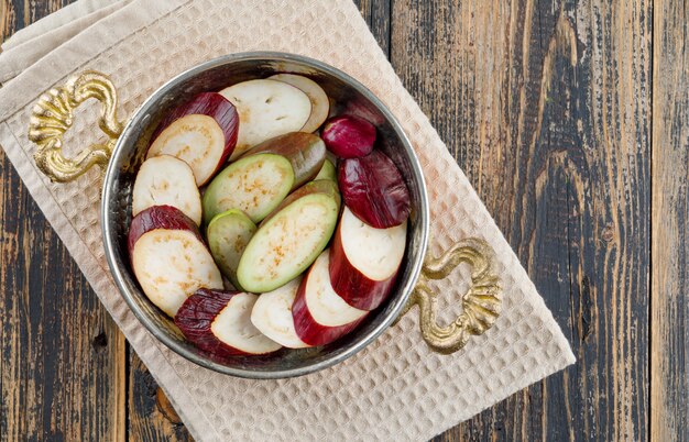 Кусочки баклажанов в сковороде на деревянных и кухонное полотенце. плоская планировка