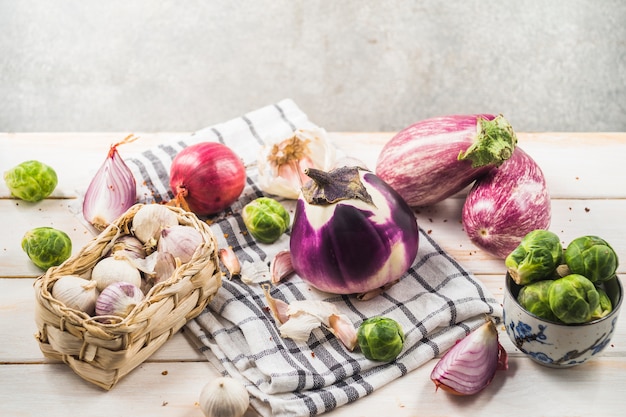 Melanzane; cavoletti di bruxelles; cipolla; spicchi d'aglio e panno sul tavolo di legno