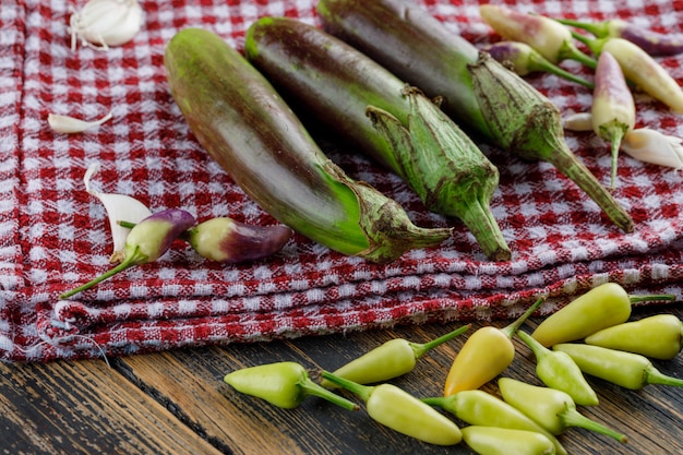 Бесплатное фото Баклажаны с чесноком, перец на деревянных и кухонное полотенце, высокий угол обзора.