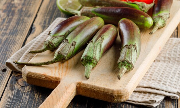 Eggplants with lime on cutting board on wooden and kitchen towel, high angle view.