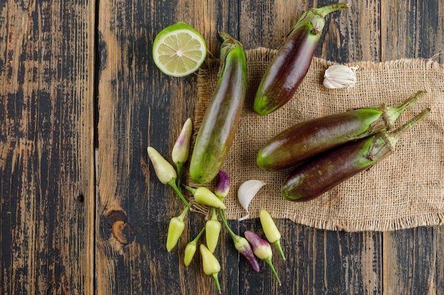 Eggplants with lime, garlic, peppers flat lay on wooden and piece of sack