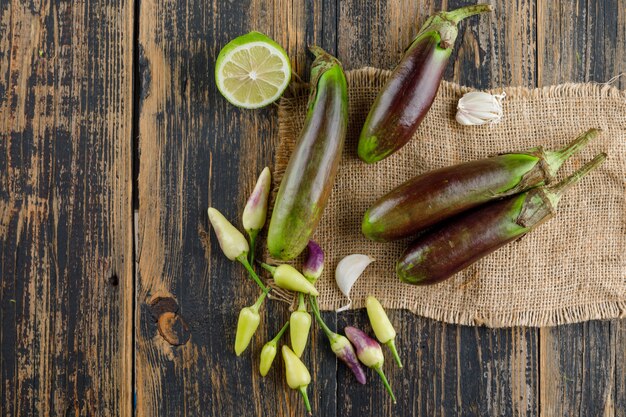 Eggplants with lime, garlic, peppers flat lay on wooden and piece of sack