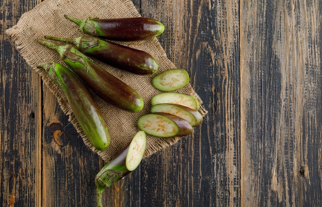 Eggplants with slices flat lay on wooden and piece of sack