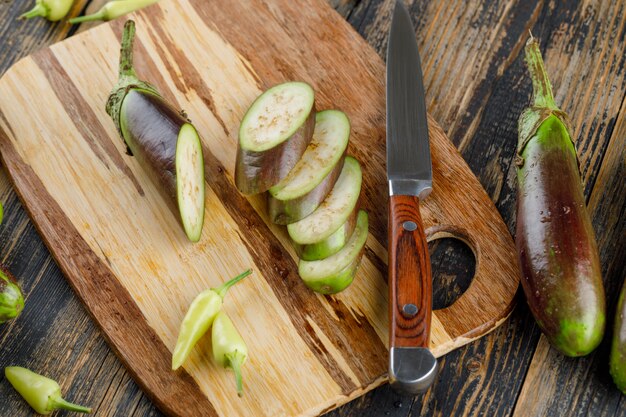 Eggplants with slices, knife, peppers flat lay on wooden and cutting board