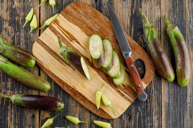 Eggplants with slices, knife, peppers on wooden and cutting board, flat lay.