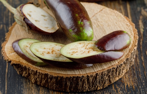 Eggplants with slices on wooden and cutting board, high angle view.