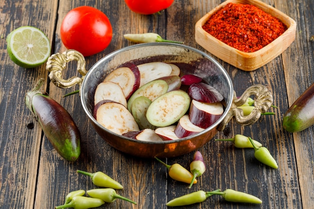 Eggplants with spice, peppers, tomatoes, lime in a pan on wooden, high angle view.