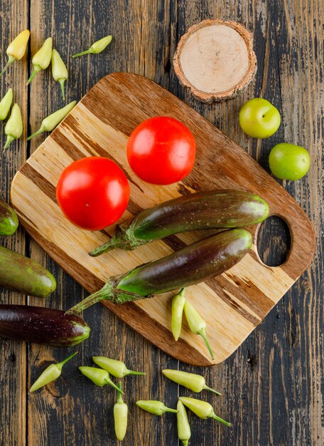 Eggplants with tomatoes, peppers, green plums, wood on wooden and cutting board, flat lay.