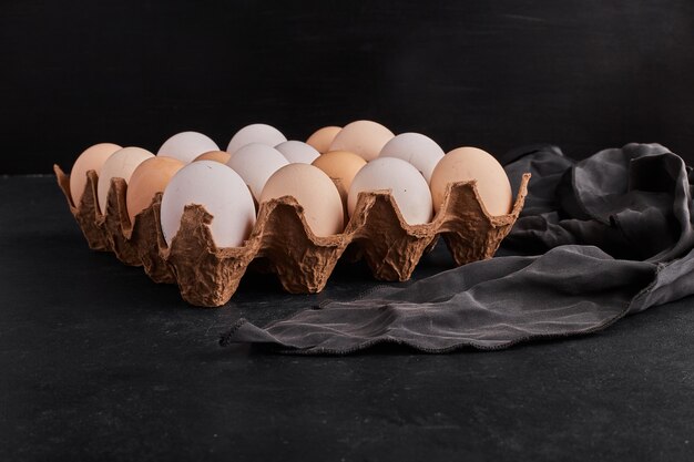 Eggs in a cardboard container on black surface. 