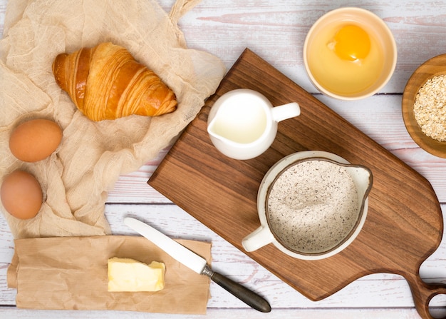 Eggs; croissant; butter; milk; flour and oats bran on wooden desk