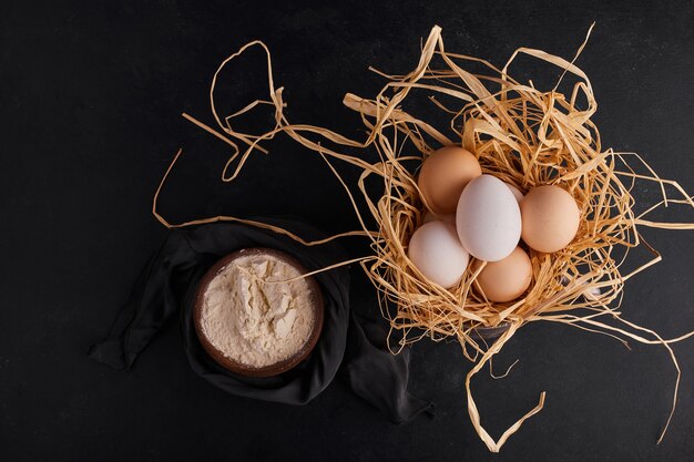 Eggs on the dry grass with a cup of flour, top view. 